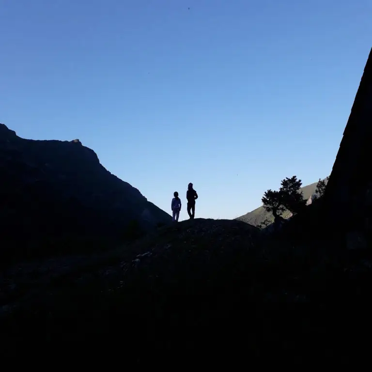 2 enfants au crépuscule à contre jour avec la montagne noire et le ciel bleu ciel