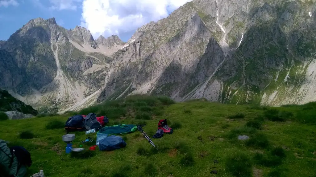 Bivouac dans l'herbe avec matériel de camping posé et sommets environnants