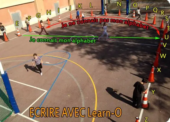 Cônes du jeu Learn-O alphabet positionnées en courbes dans le sens des lettres de l'alphabet avec des élèves jouant dans la cour de l'école