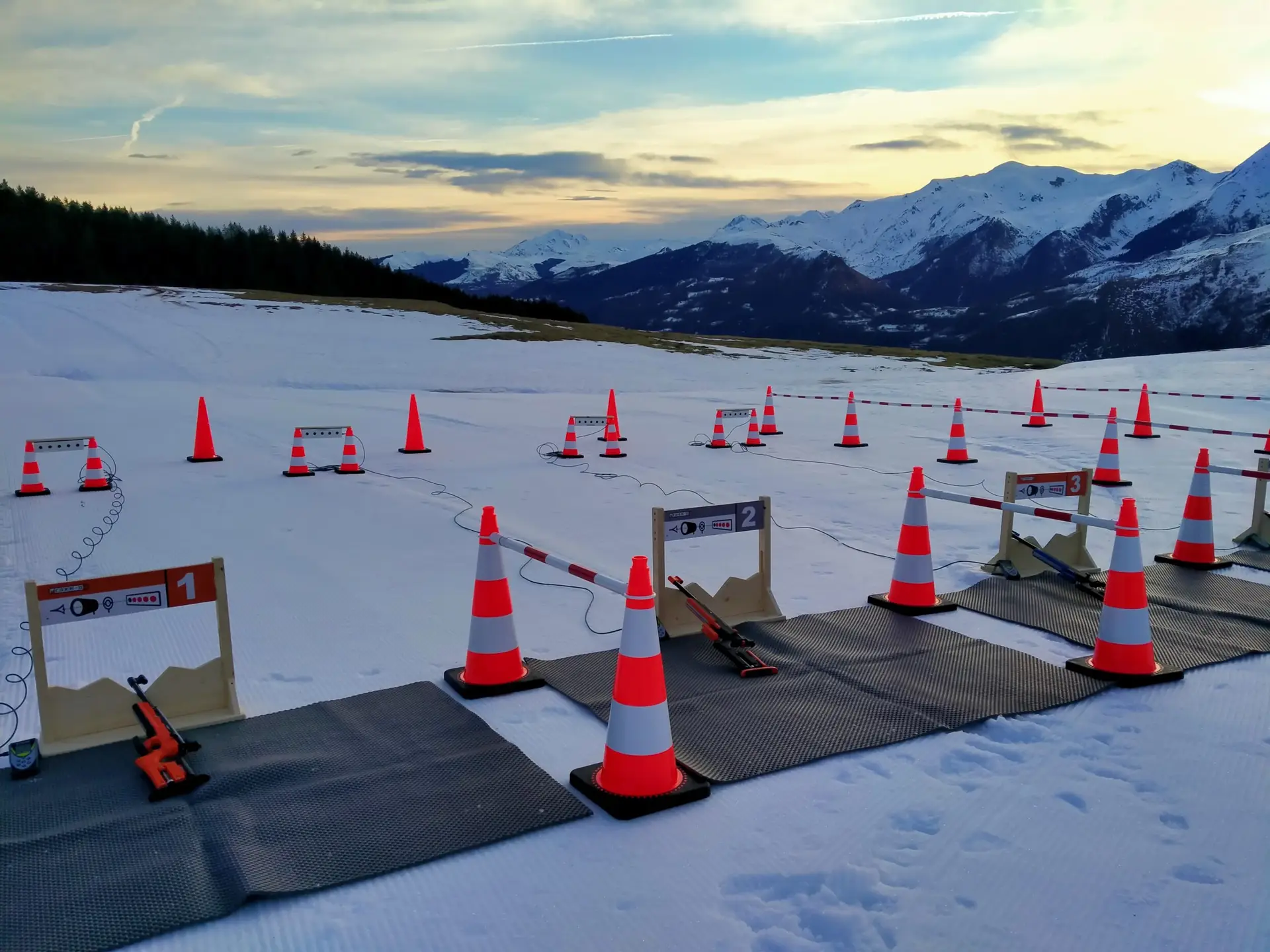 Installation du pas de tir de biathlon au Col du Soulor avec les tapis de sol, les cônes et les carabines optiques dans la neige