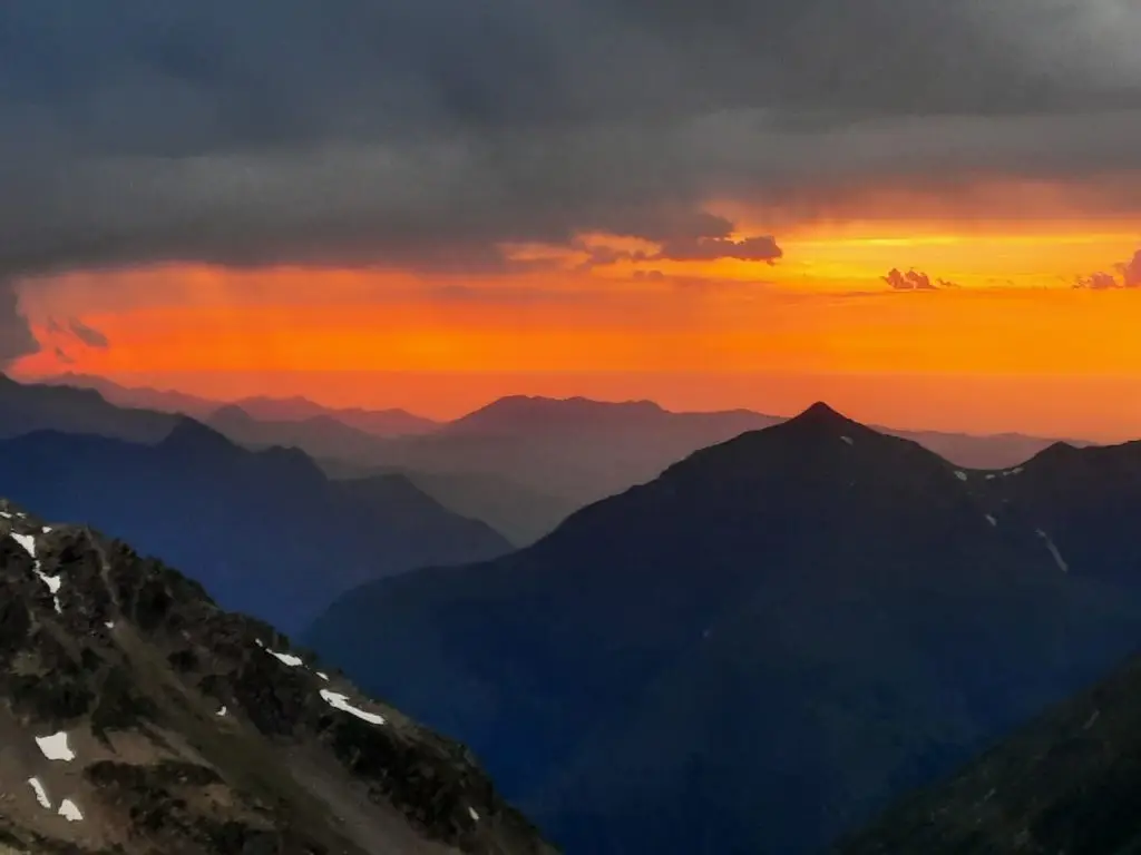 Ciel rougeoyant avec un panorama de montagnes au coucher du bivouac dans le Néouvielle avec quelques plaques de neige visibles sur un flanc de montagne