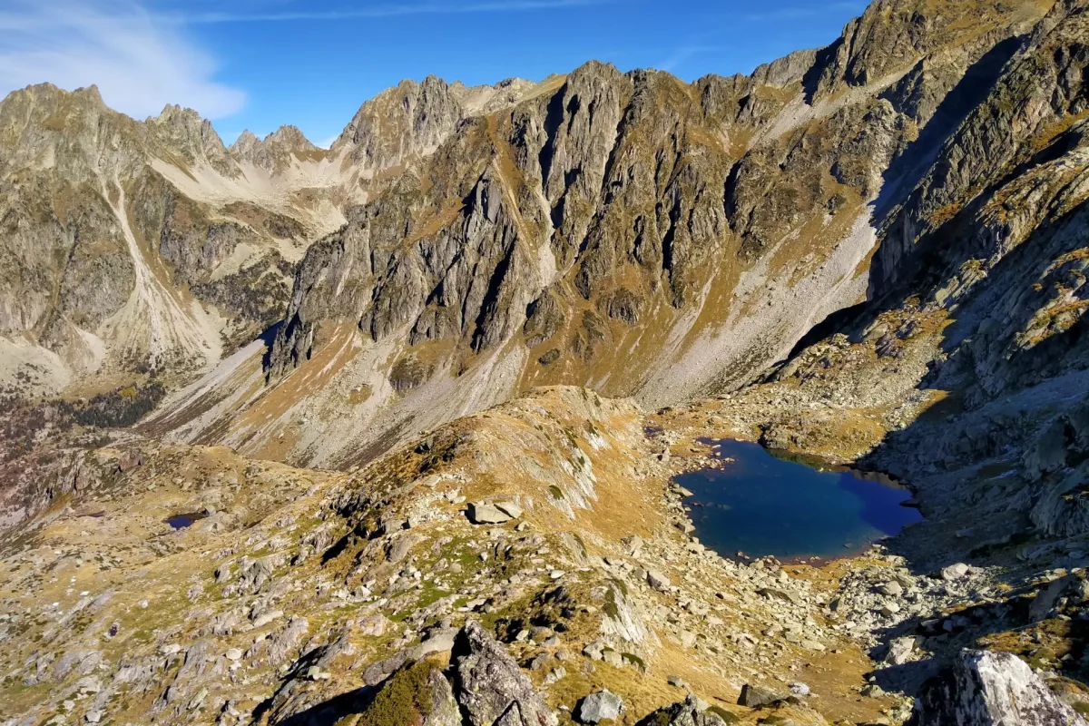 Lac de montagne accroché au flanc de la montagne dans un petit vallon, sommets en fond