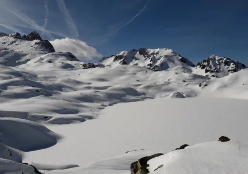 Lac recouvert par la neige avec des sommets en fond et un ciel bleu