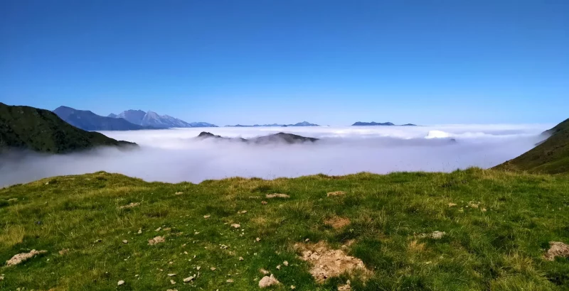 Vue depuis une estive sur une mer de nuage avec un ciel bleu et des sommets à l'horizon