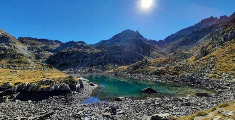 Soleil au milieu du ciel bleu se reflétant dans un lac de montagne val d'azun tour des lacs