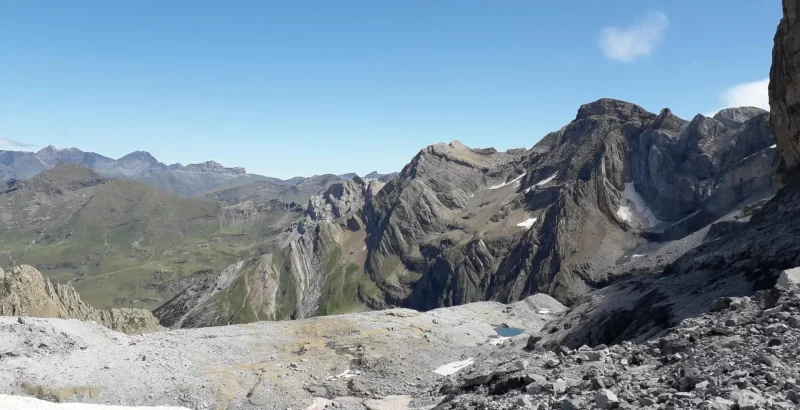 Vue sur le pic du Marboré et ses plissures depuis le glacier des Sarradets. Ambiance minérale au premier plan, avec un laquet et estives verdoyantes des espuguettes au fond de l'image