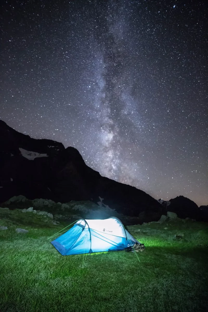 Tente de bivouac éclairée sur l'herbe dans la nuit surplombée par la voie lactée